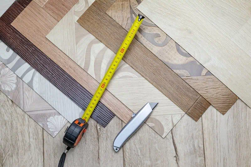 Vzorky podlahového materiálu s metrem a nožem na řezání.