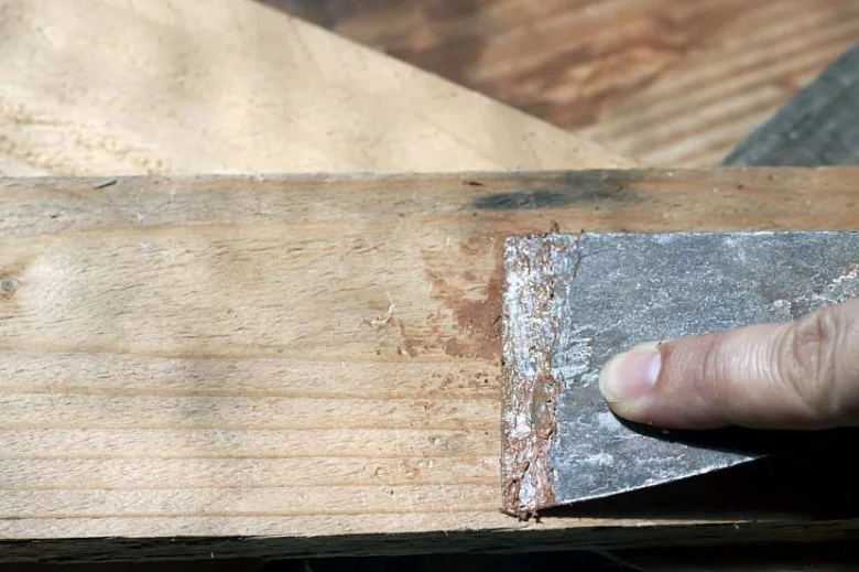 Ruční škrabka odstraňuje starý materiál z praskliny v dřevěném trámu.