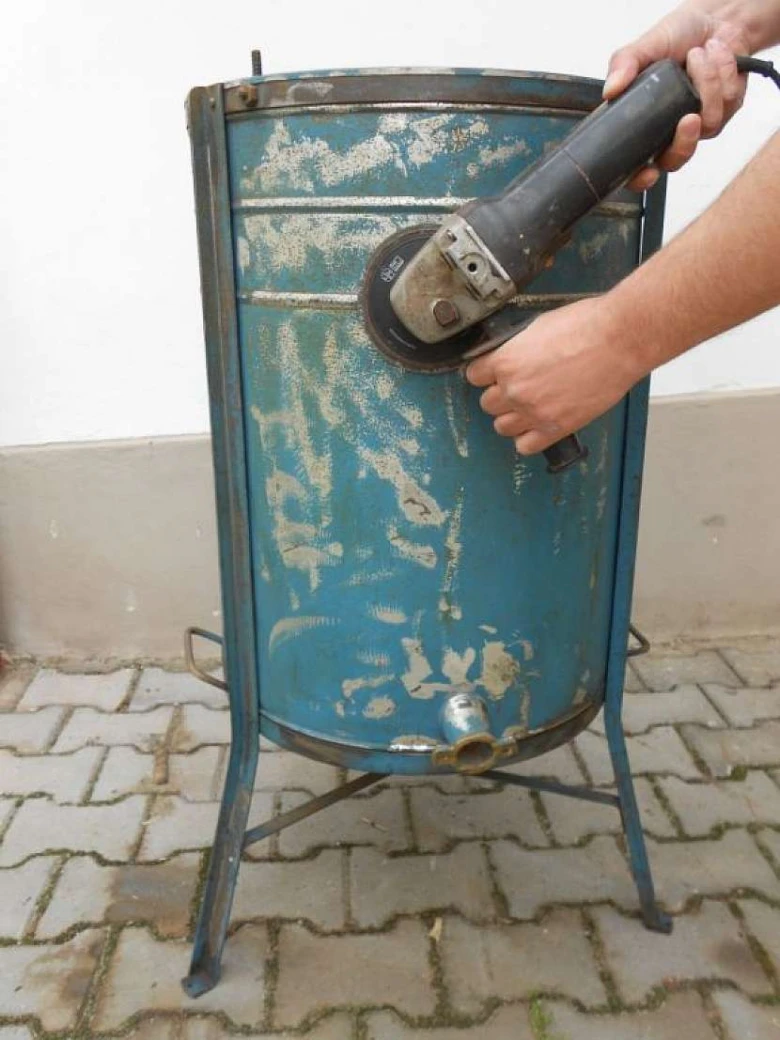 Muž škrábe starou smaltovanou vanu bruskou.