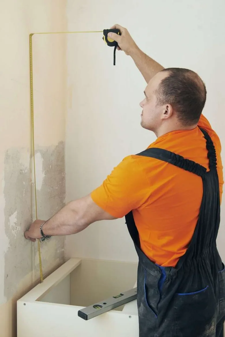 Muž měří stěnu pro zavěšení kuchyňských skříněk