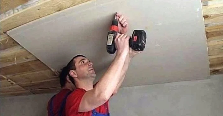 Muž upevňuje sádrokarton šrouby na stropní trámy.