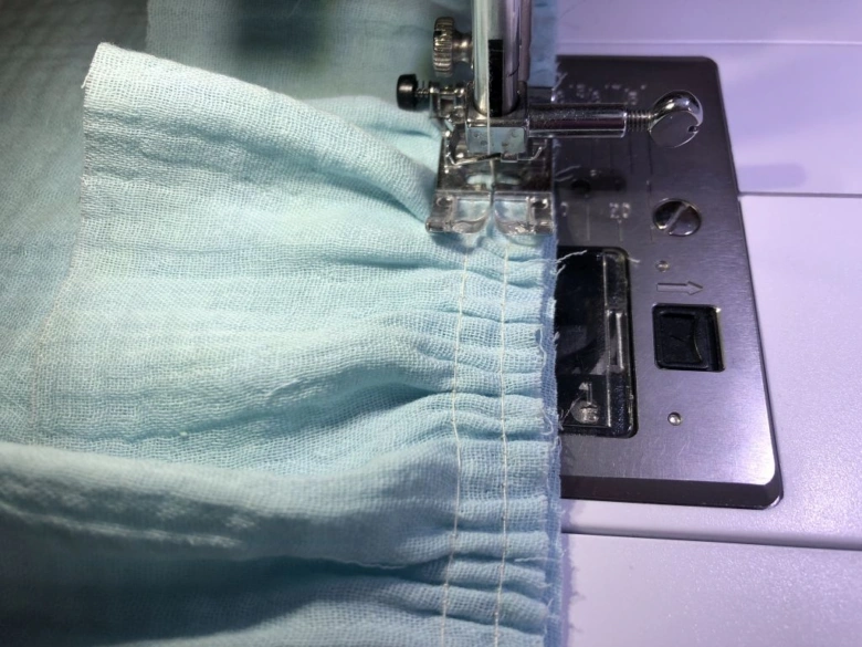 Šicí stroj šije světle modrý textil pro sbíhání látky.