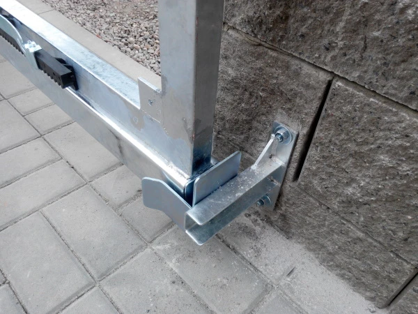 Kovová montážní konzole pro posuvnou bránu na kamenné zdi.