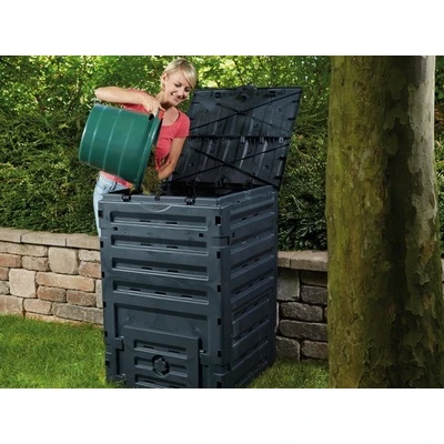 Žena přisypává kompost do černého plastového boxu na zahradě.