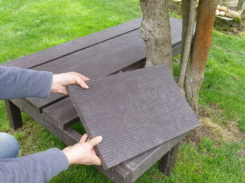 Člověk montuje tmavé prkna na zahradní lavičku ze dřeva.