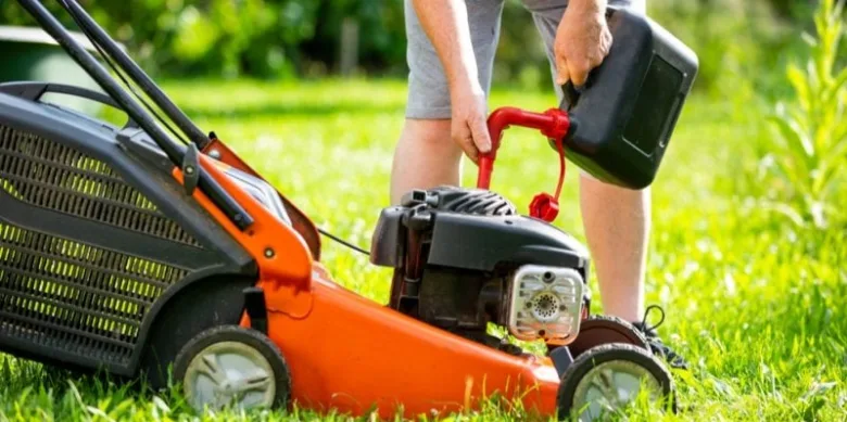 Muž nalévá benzín do motoru sekačky na trávu.