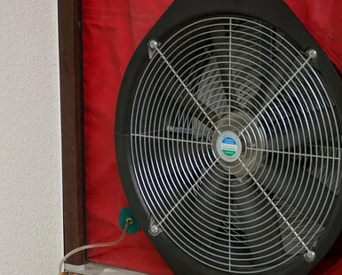 Velký průmyslový ventilátor s červeným krytem na zdi.