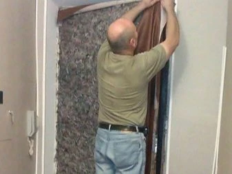 Muž čalouní dveře vlastníma rukama a aplikuje látku.