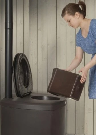 Žena vkládá krabici rašeliny do kompostovací toalety.