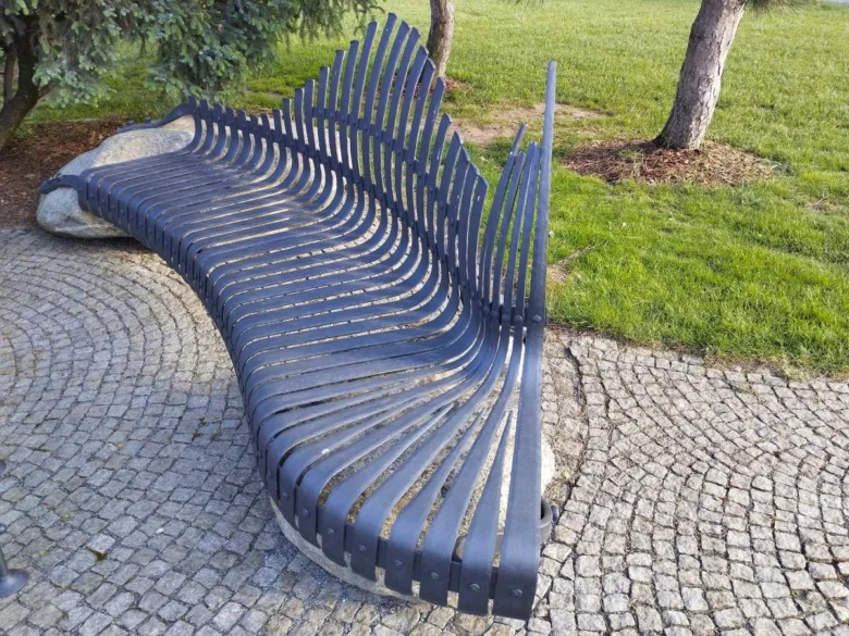 Moderní zakřivená kovová lavička v parku na dlažbě.