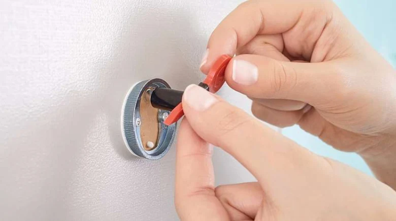 Ruční instalace červeného přísavkového háčku na bílou stěnu.