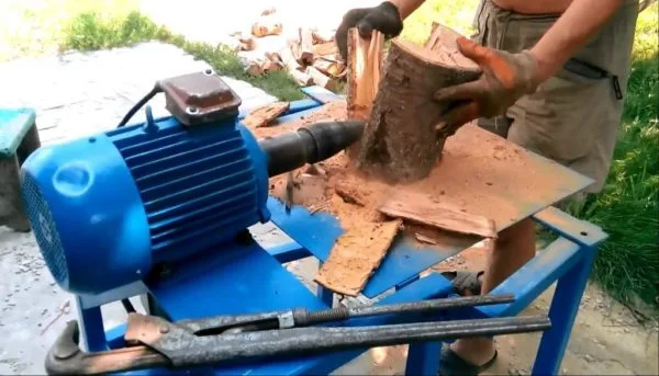 Muž štípí dřevo na domácí štípačce s modrým motorem.