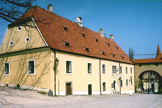 Žlutá budova zámku s červenou střechou a vstupní branou.