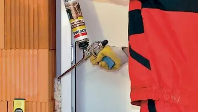 Pracovník zalepuje otvor v plastovém okenním rámu těsnicí hmotou.