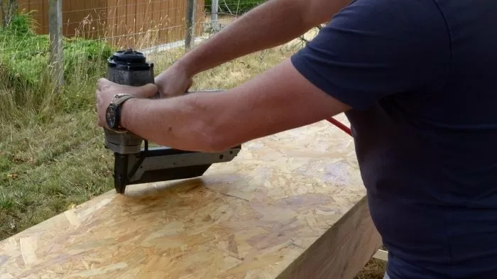Muž používá hřebíkovačku na dřevěné desce venku.