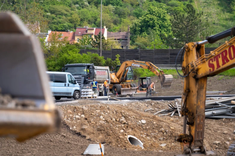 Žluté bagry na staveništi s pracovníky v ochranném oblečení.