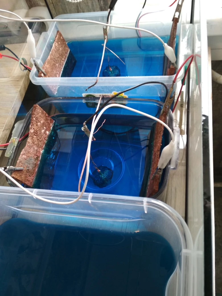 Domácí pokovování mědi s elektrodami v modrém roztoku.