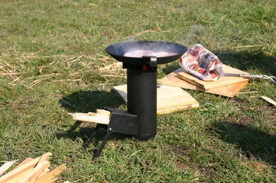 Černá raketová kamna venku s pánví na trávníku.