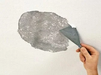Ruka nanáší šedou omítku na stěnu malířským nástrojem.
