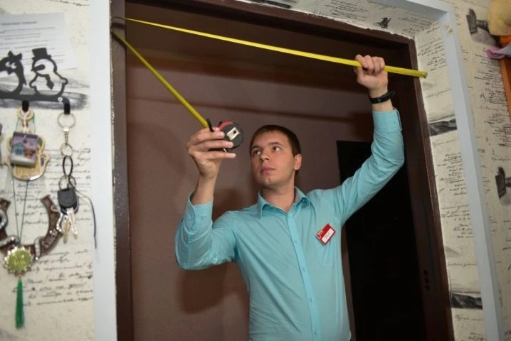 Muž měří rámeček dveří páskou pro izolaci.