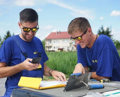 Dva muži pracují venku s mobilními zařízeními a nástroji.