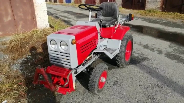 Červený minitraktor KMZ 012 na štěrkové ploše.