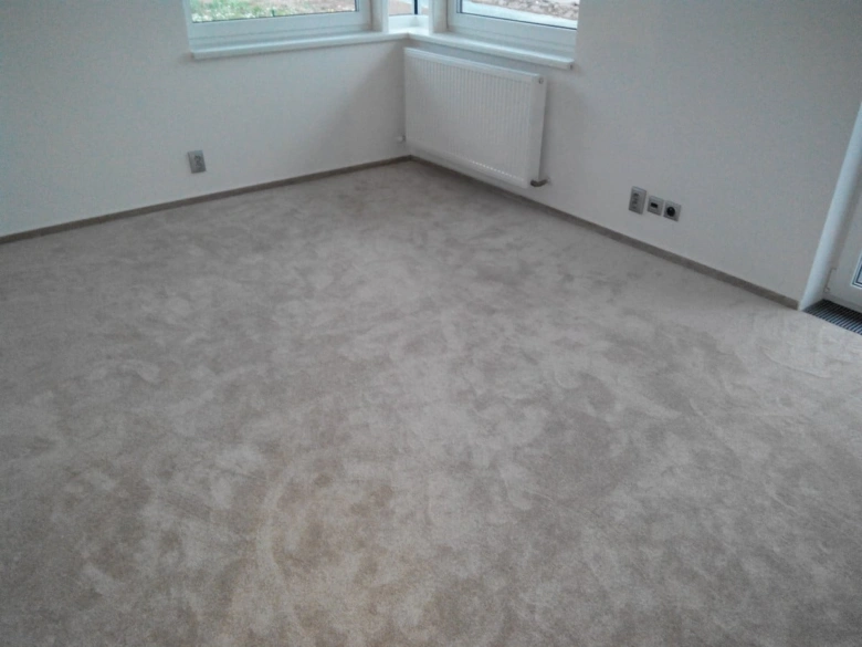 Koberlec položený na betonové podlaze v prázdné místnosti.