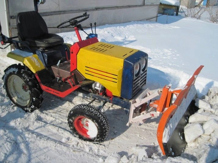 Mini traktor s oranžovým odhazovačem sněhu v zimním prostředí.