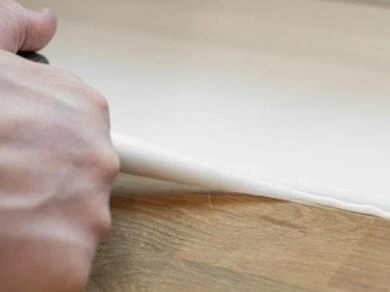 Ruka přitiskuje bílý plast na povrch při lepení.