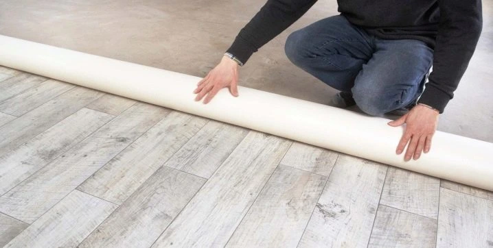 Muž položí bílý linoleum na dřevěnou podlahu vlastními rukama.