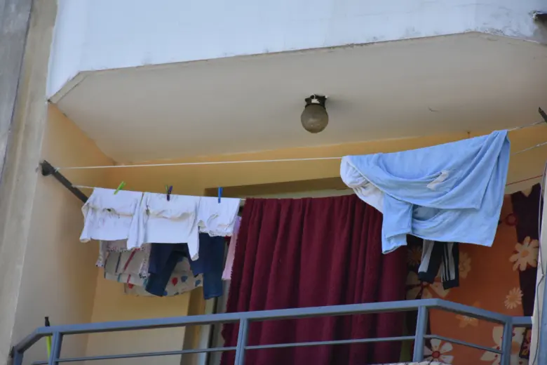 Prádlo visí na šňůře na balkóně s viditelnými háčky.