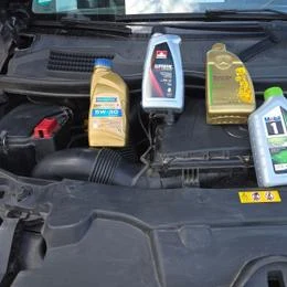 Různé lahve s motorem olejem na kapotě auta pro výběr správného oleje.