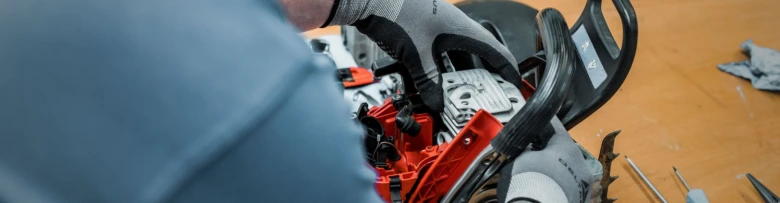Ruční demontáž motorové pily s nářadím na pracovním stole.