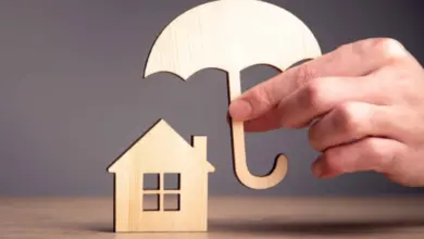 Ruka drží nad dřevěným domkem stříšku jako ochrana proti riziku.