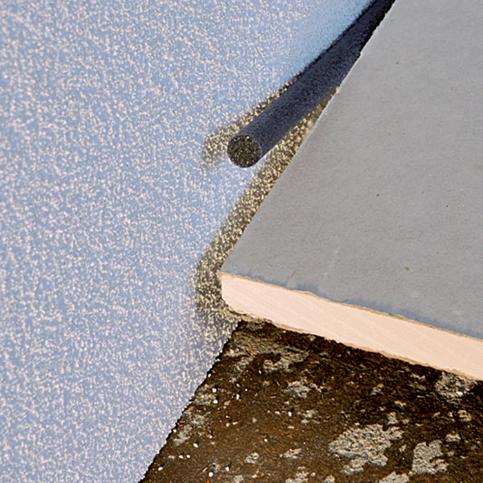 Detail utěsnění spáry mezi dvěma kusy linoleumu tmavým těsnicím materiálem.