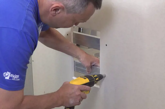 Muž opravuje sádrokarton bez použití profilu pomocí vrtáku.