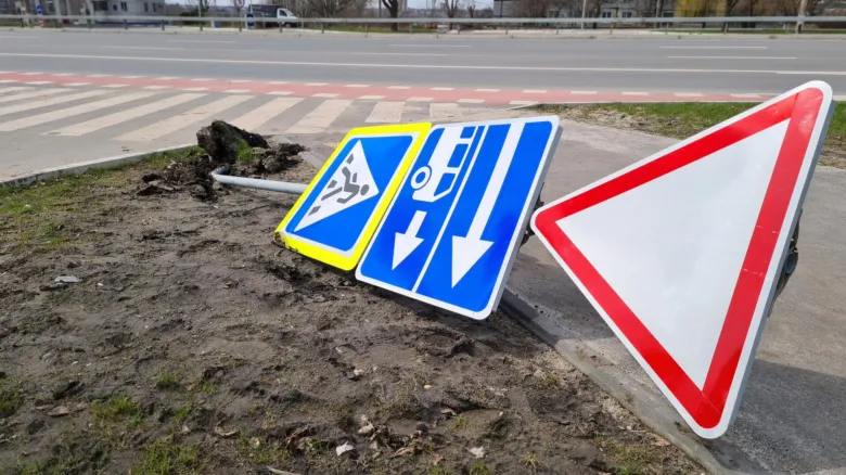 Poškozené dopravní značky leží v blátivém příkopu vedle silnice.
