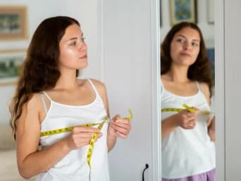 Žena měří velikost hrudníku páskou před zrcadlem.