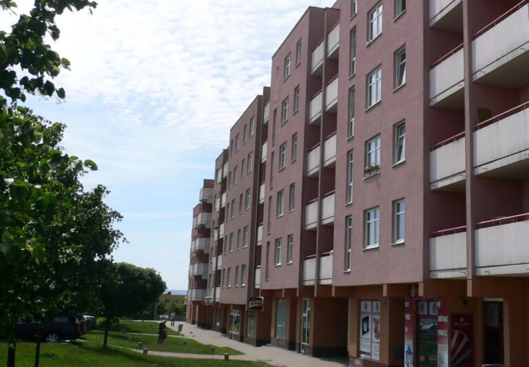 Řada bytových domů s balkony vedle zelené trávníkové plochy.