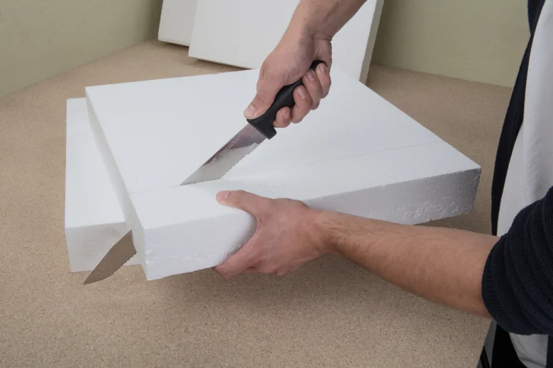 Muž řezí bílou desku z expandovaného polystyrenu nožem.