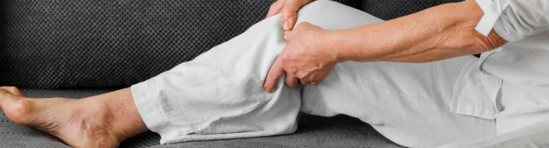 Muž drží své bolavé koleno při sedění na gauči.