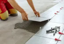 Montáž dlaždice na podlahu s použitím lepidla a roztečných kousků.