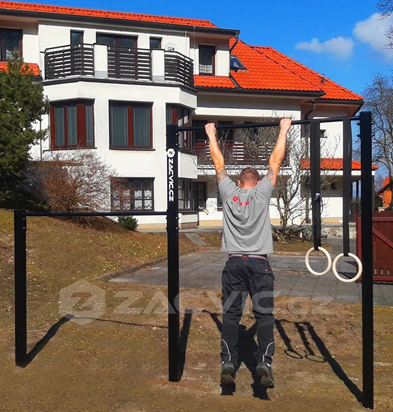 Muž visí na hrazdi venku před domem.