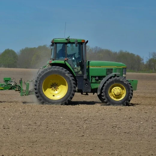 Zelený traktor s připojeným pługem na orané poli.