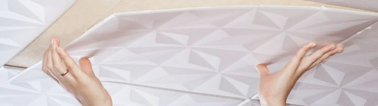 Ruce drží bílou stropní desku z expandovaného polystyrenu.