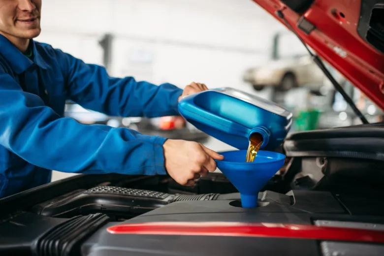 Mechanik nalévá olej do motora auta v dílně.