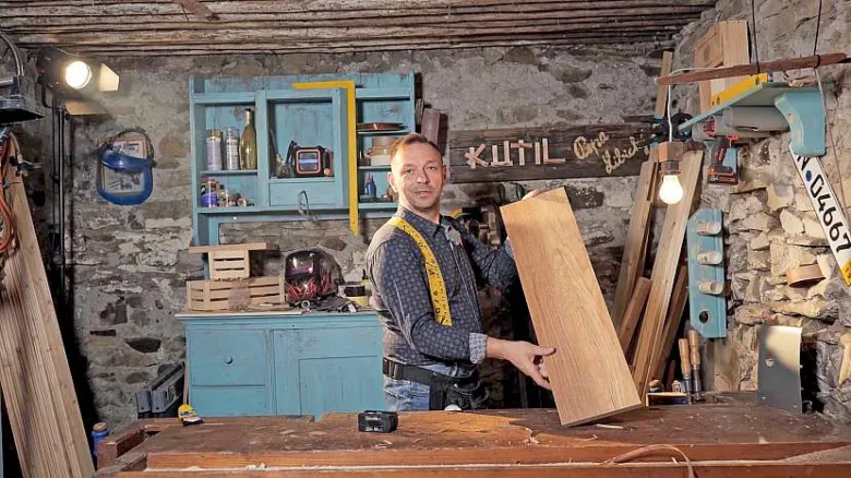 Muž drží dřevěnou prkno v dílně s nářadím.