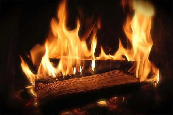 Hořící kus dřeva s plameny v krbu nebo kamnech.