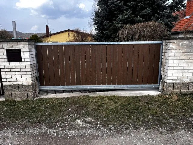 Posuvná brána mezi cihlovými sloupy na pozadí trávníku.