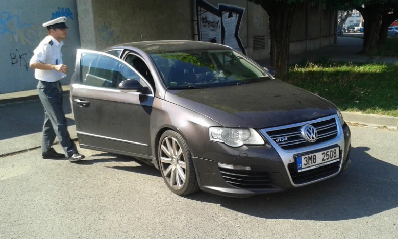 Český policista stojí u vozu s otevřenou dveřmi na ulici.